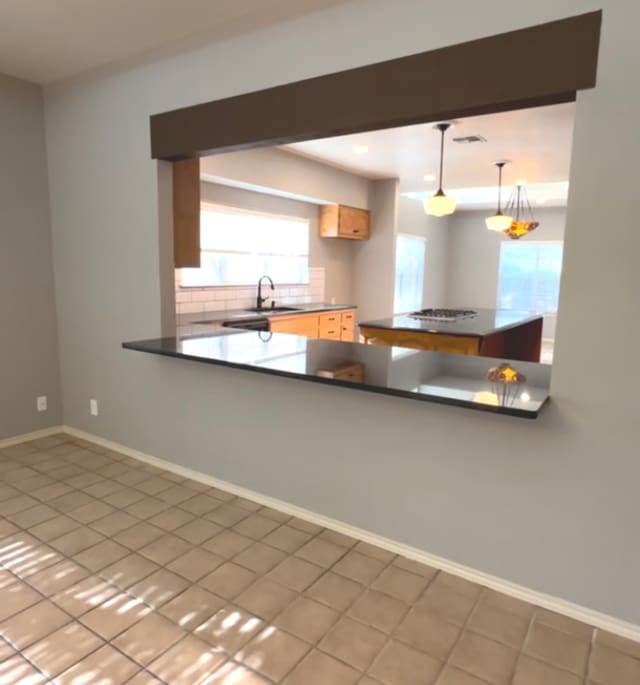 kitchen with backsplash, tile patterned floors, sink, light brown cabinets, and decorative light fixtures