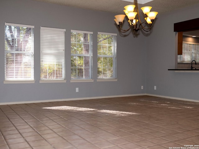 empty room featuring tile patterned flooring, plenty of natural light, a textured ceiling, and a notable chandelier