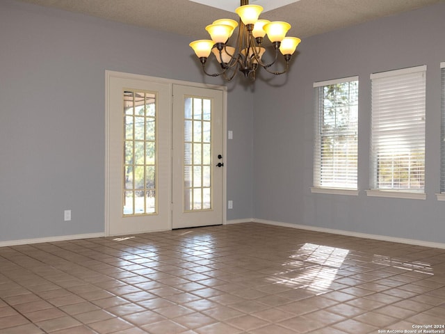 unfurnished room with tile patterned floors, a healthy amount of sunlight, a textured ceiling, and a chandelier