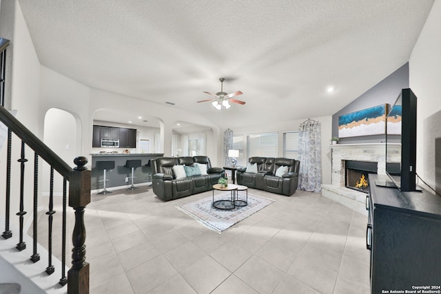 living room with ceiling fan, a premium fireplace, vaulted ceiling, a textured ceiling, and light tile patterned floors