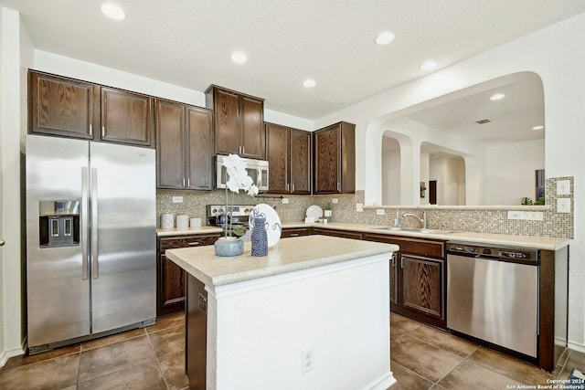 kitchen with sink, kitchen peninsula, decorative backsplash, dark brown cabinets, and appliances with stainless steel finishes