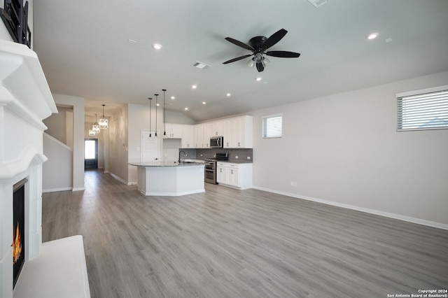 kitchen featuring light wood-type flooring, stainless steel appliances, decorative light fixtures, white cabinets, and an island with sink