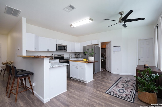 kitchen with white cabinets, butcher block countertops, a kitchen bar, kitchen peninsula, and stainless steel appliances