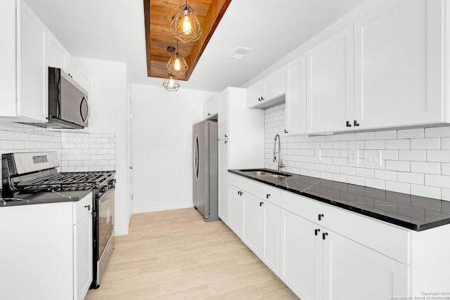 kitchen featuring sink, backsplash, appliances with stainless steel finishes, white cabinets, and light wood-type flooring