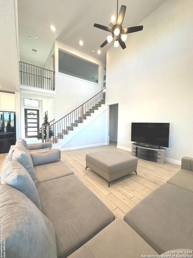 living room with a high ceiling, light hardwood / wood-style flooring, and ceiling fan