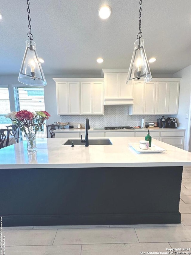 kitchen featuring a center island with sink, sink, decorative backsplash, decorative light fixtures, and white cabinetry