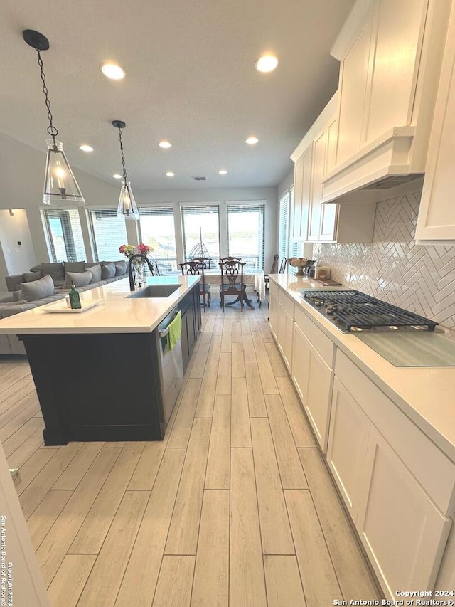 kitchen with light wood-type flooring, sink, pendant lighting, a center island with sink, and white cabinets