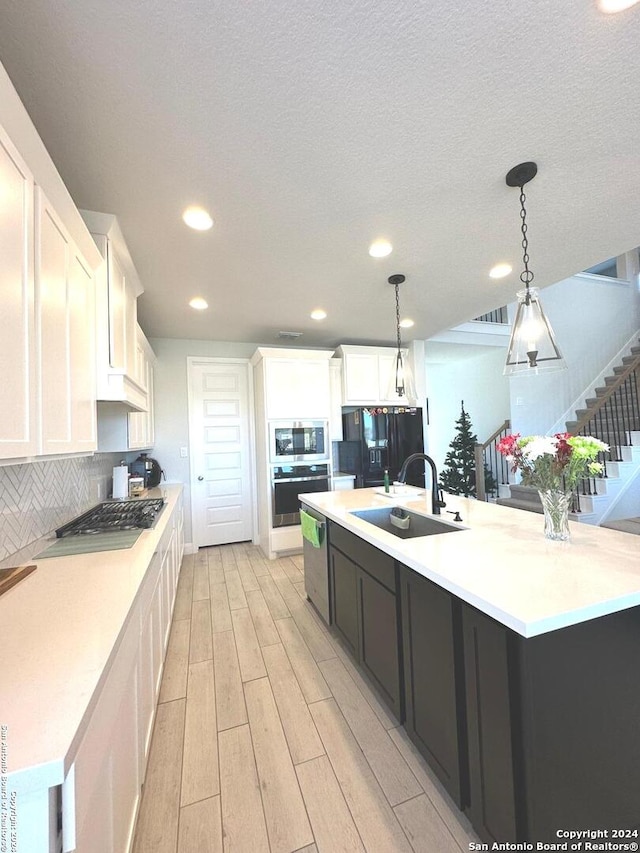 kitchen with stainless steel appliances, white cabinets, hanging light fixtures, and light wood-type flooring