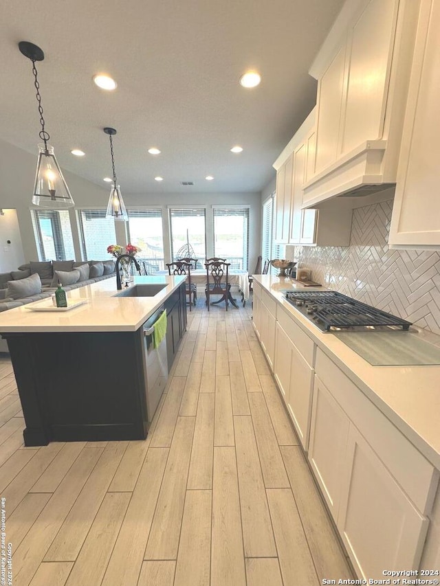 kitchen featuring appliances with stainless steel finishes, light wood-type flooring, pendant lighting, white cabinetry, and an island with sink