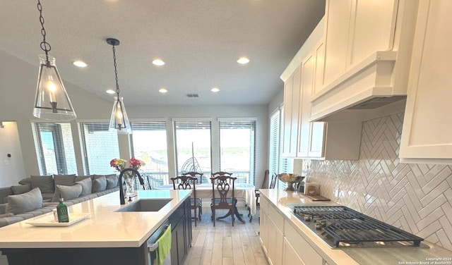 kitchen with white cabinetry, decorative light fixtures, a kitchen island with sink, appliances with stainless steel finishes, and light wood-type flooring