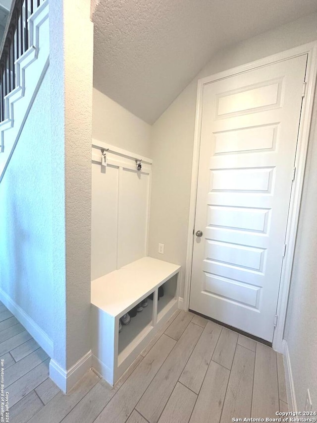 mudroom featuring light hardwood / wood-style floors, a textured ceiling, and vaulted ceiling