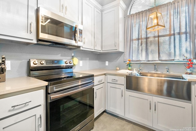 kitchen featuring sink, hanging light fixtures, light tile patterned floors, white cabinetry, and stainless steel appliances