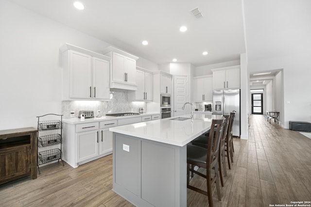 kitchen with white cabinets, sink, light hardwood / wood-style flooring, an island with sink, and stainless steel appliances