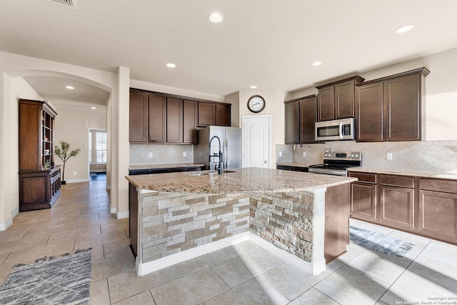 kitchen with sink, light stone counters, stainless steel appliances, and a kitchen island with sink