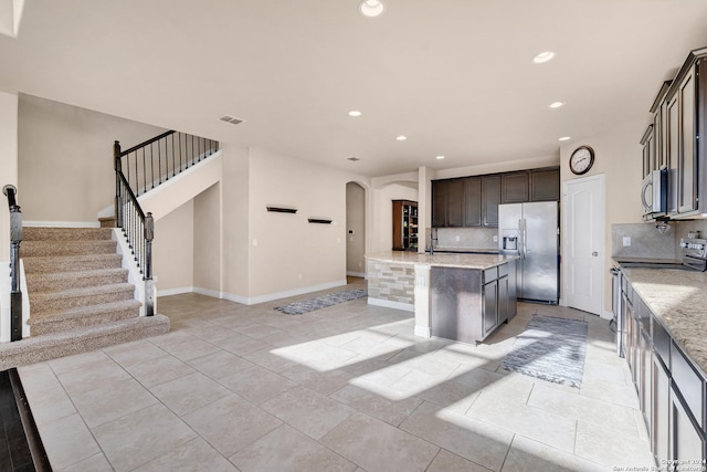 kitchen with decorative backsplash, dark brown cabinets, stainless steel appliances, and an island with sink