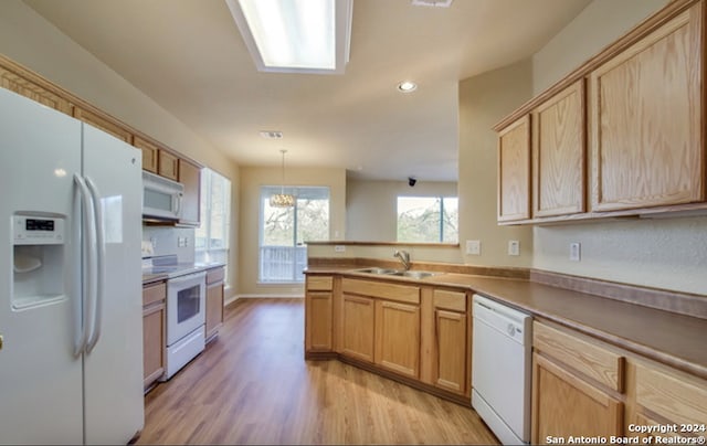 kitchen with kitchen peninsula, light wood-type flooring, white appliances, sink, and decorative light fixtures