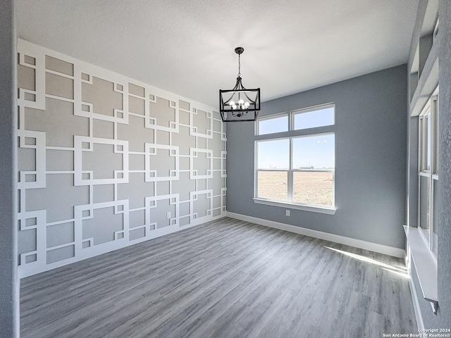 empty room featuring a chandelier, wood-type flooring, and a textured ceiling