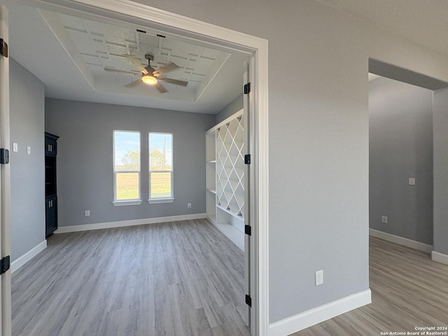 interior space with a raised ceiling, light hardwood / wood-style flooring, and ceiling fan