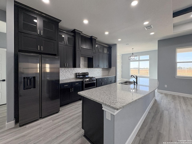 kitchen featuring decorative backsplash, appliances with stainless steel finishes, a kitchen island with sink, sink, and light hardwood / wood-style flooring