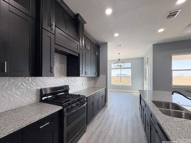 kitchen with sink, stainless steel gas stove, light wood-type flooring, tasteful backsplash, and light stone counters