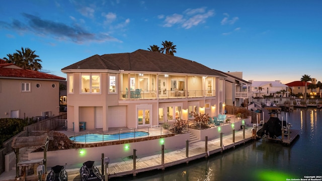 back house at dusk with a patio, a balcony, and a water view