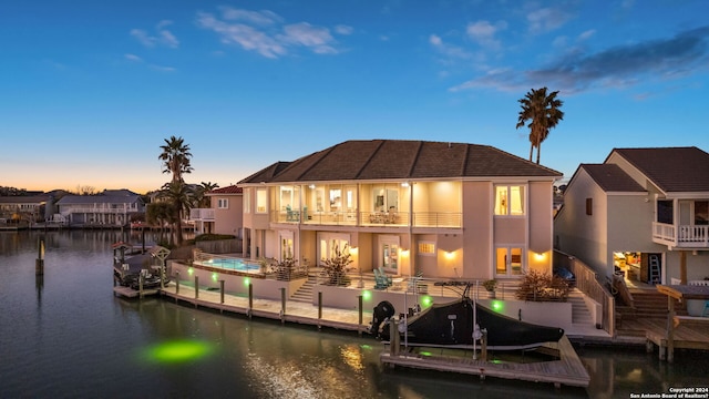 back house at dusk with a balcony and a water view