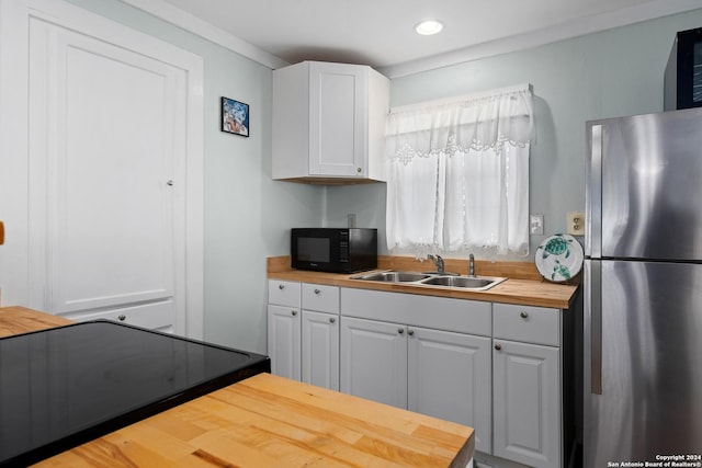 kitchen with stove, sink, stainless steel fridge, white cabinetry, and butcher block counters
