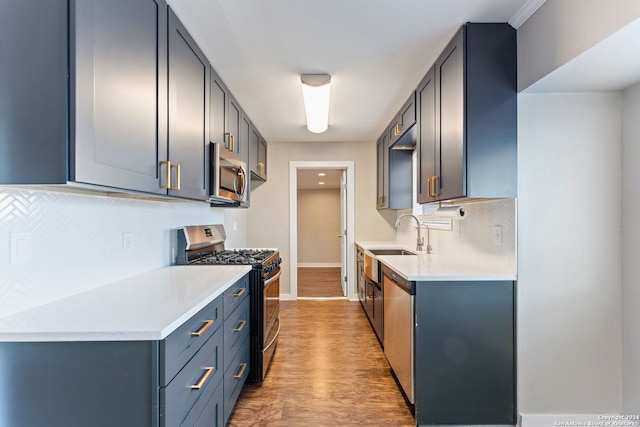 kitchen with backsplash, blue cabinets, sink, wood-type flooring, and stainless steel appliances