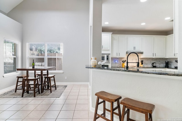 kitchen with light tile patterned floors, backsplash, white cabinetry, and dark stone countertops