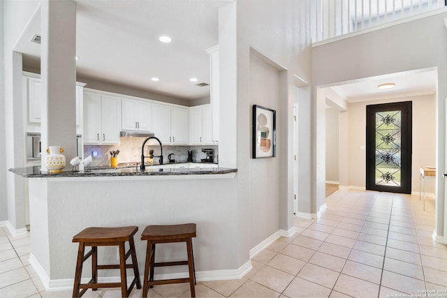 kitchen with white cabinets, dark stone countertops, kitchen peninsula, and backsplash