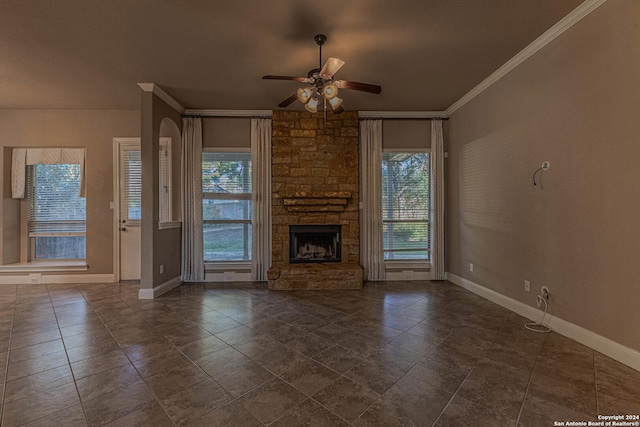 unfurnished living room with plenty of natural light, ceiling fan, a stone fireplace, and ornamental molding