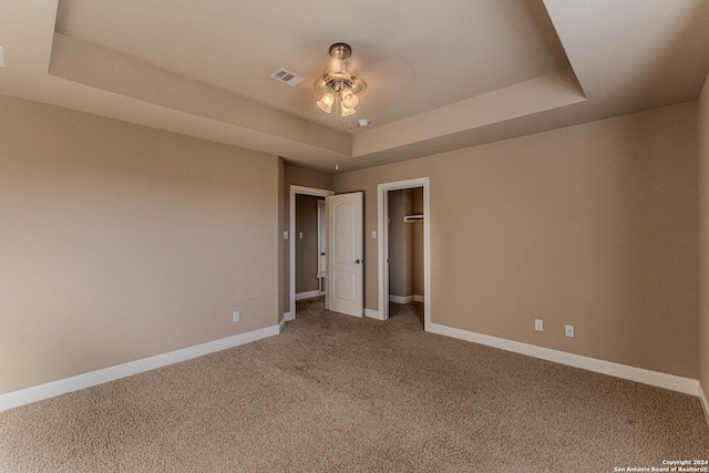 unfurnished bedroom with ceiling fan, a raised ceiling, and carpet floors