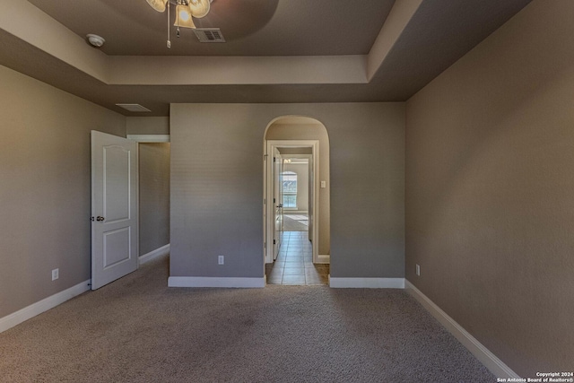 spare room with ceiling fan, a raised ceiling, and light carpet