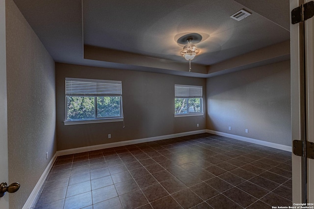 unfurnished room with dark tile patterned flooring, ceiling fan, a textured ceiling, and a tray ceiling