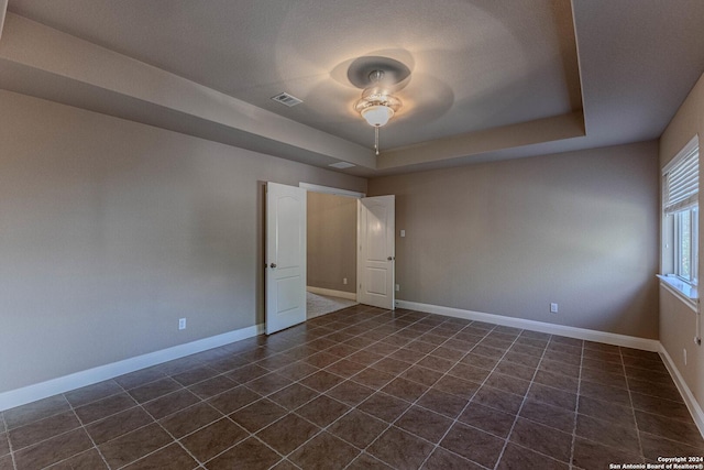 tiled spare room featuring a raised ceiling and ceiling fan