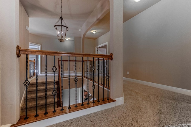 stairway with carpet floors and an inviting chandelier