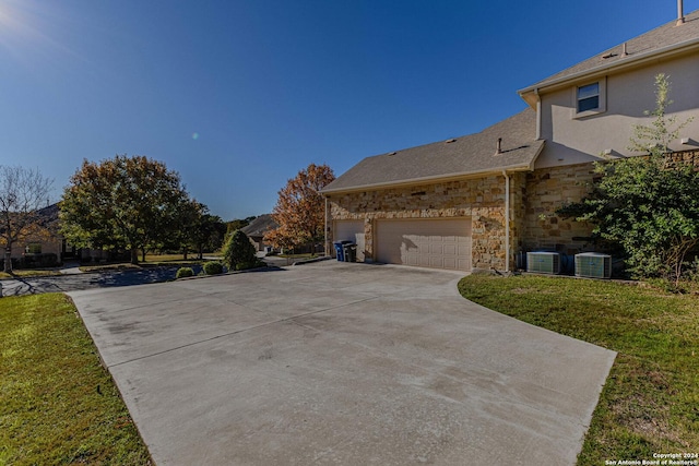 view of side of property featuring a lawn, a garage, and central AC