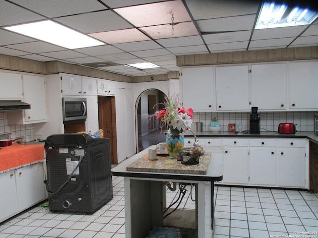 kitchen featuring decorative backsplash, a drop ceiling, white cabinets, and light tile patterned floors