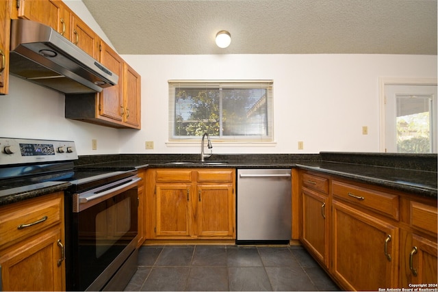 kitchen with dark tile patterned flooring, sink, a textured ceiling, appliances with stainless steel finishes, and range hood