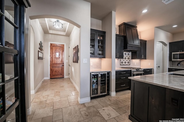 kitchen with light stone countertops, stainless steel appliances, a raised ceiling, wine cooler, and decorative backsplash