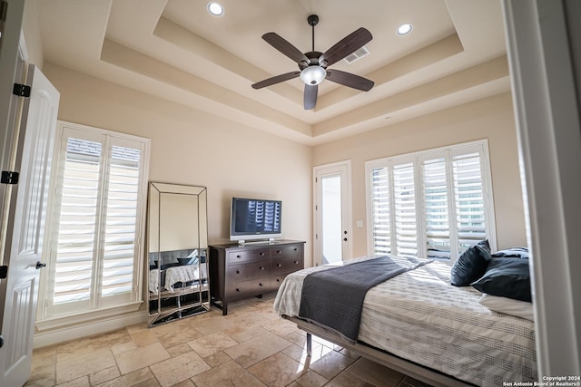 bedroom featuring ceiling fan, a tray ceiling, and multiple windows