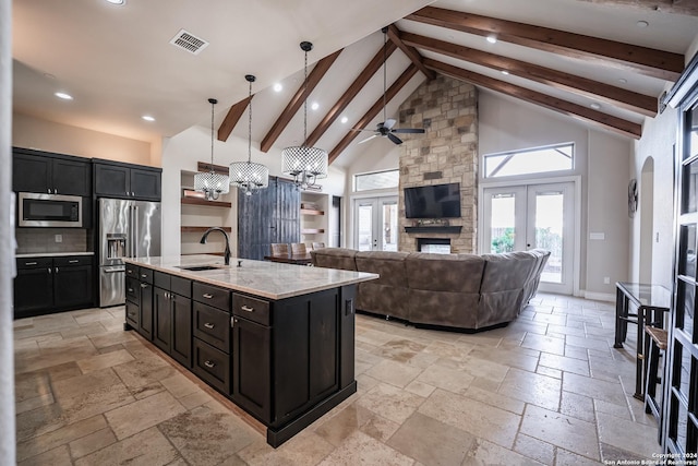 kitchen with appliances with stainless steel finishes, a kitchen island with sink, sink, beamed ceiling, and hanging light fixtures