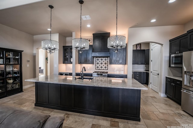 kitchen with light stone countertops, sink, stainless steel appliances, pendant lighting, and a kitchen island with sink