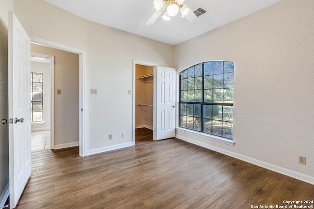 unfurnished bedroom with a walk in closet, multiple windows, and dark wood-type flooring