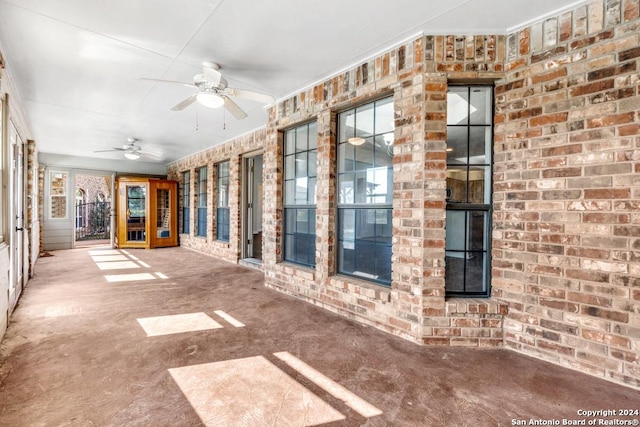 unfurnished living room with ceiling fan and brick wall