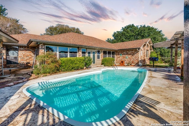 pool at dusk with a patio area and a grill