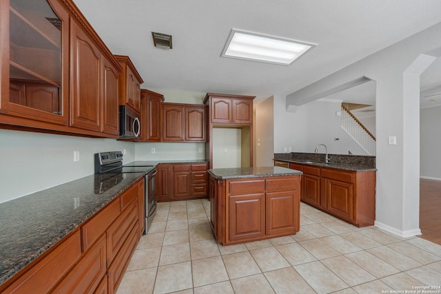 kitchen with a center island, dark stone counters, sink, light tile patterned floors, and appliances with stainless steel finishes