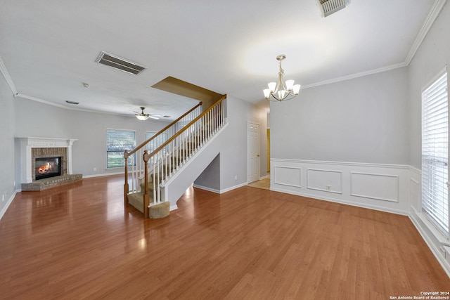 unfurnished living room with a fireplace, wood-type flooring, ceiling fan with notable chandelier, and ornamental molding