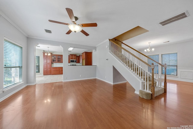 unfurnished living room featuring ceiling fan with notable chandelier, light hardwood / wood-style floors, and crown molding