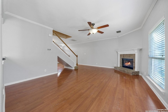 unfurnished living room with wood-type flooring, a brick fireplace, ceiling fan, and ornamental molding